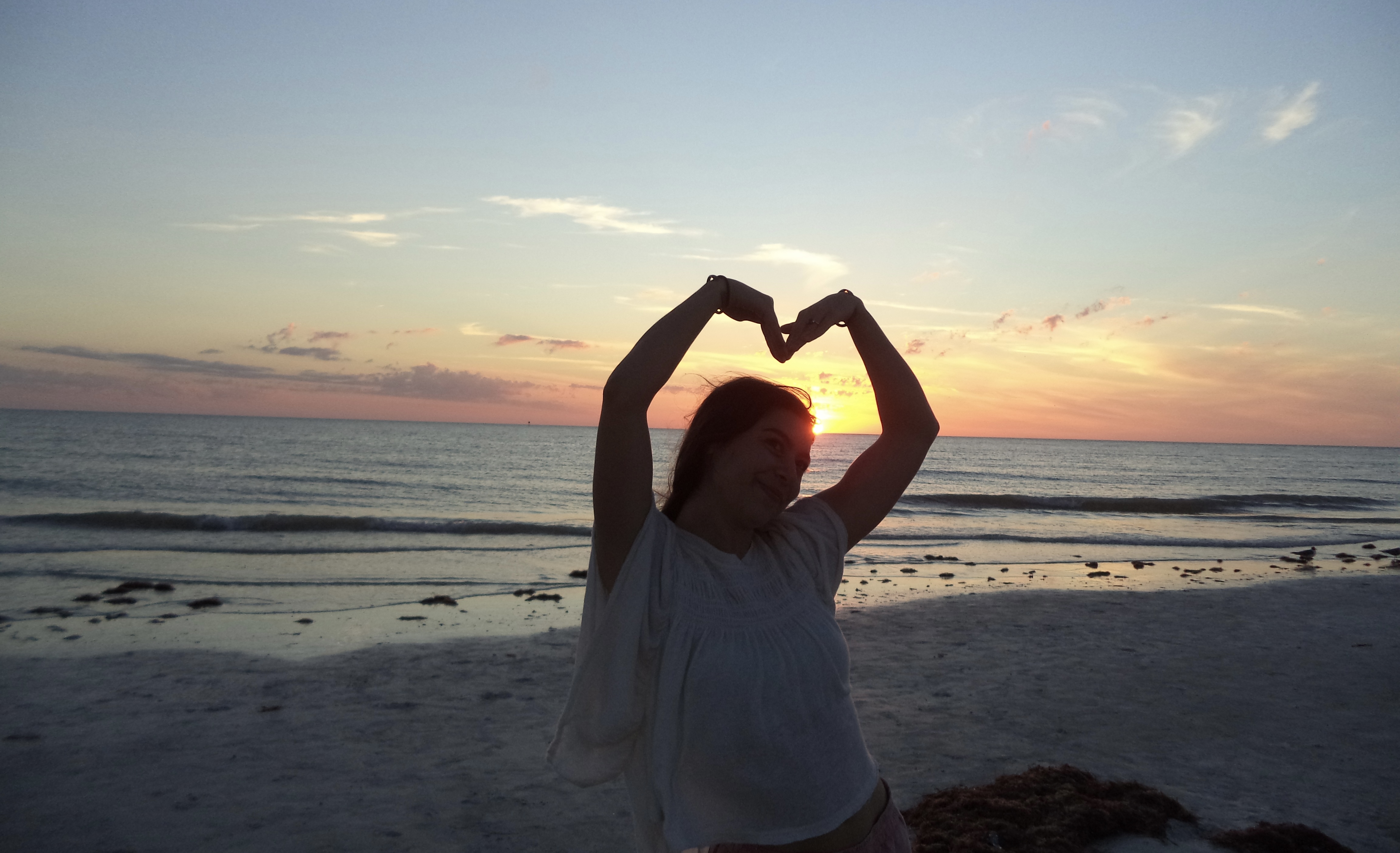 Woman making a heart at sunset — love as a call to action