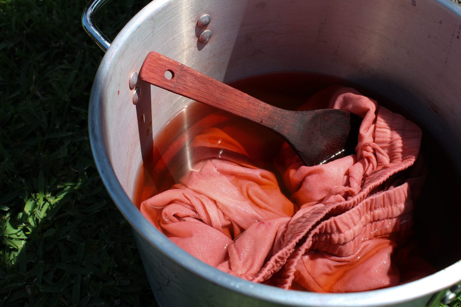 Fabric steeping in a pot of natural plant dye, rich coral color